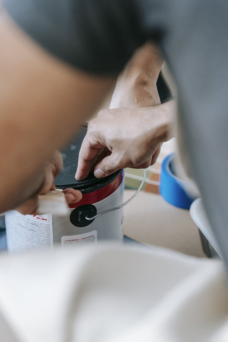 Close-up of a man opening a paint can, preparing for a home renovation with painting materials nearby.